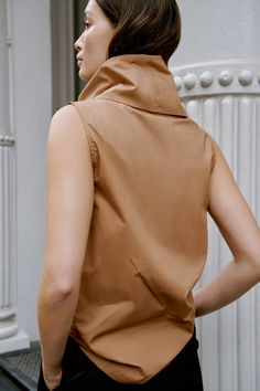 Make a statement with the Marcy Sleeveless Top, a structured and sleek shirt that transforms into a turtleneck. Marcy's unique turtleneck can be worn in two ways — fold in half to wear it gathered at the neckline, or amp up the oversize by standing up the collar for free-form volume. Crafted from 100% European poplin cotton, Marcy provides effortless day-to-night styling possibilities. [SPLIT] Yada, in chestnut, is 5'9" (175 cm) tall, wearing size XS. Sam, in light beige, is 5'8" (173 cm) tall, Chic High Neck Cotton Tops, Chic High Neck Tank Top For Fall, High Neck Vest Top For Spring, Chic Sleeveless Tops For Fall, Chic Brown Vest Top, Fitted Turtleneck Vest For Spring, Spring Turtleneck Vest, Brown High Neck Top For Work, Sleeveless Blouse For Fall Layering