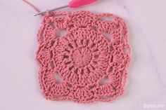 the crochet square is being worked on with a pink yarn needle and thread