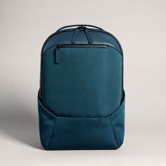 a blue backpack sitting on top of a white floor next to a gray wall with a black zipper