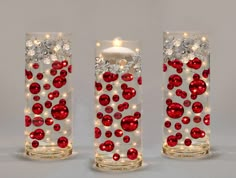 three glass vases with red and white ornaments on the sides, one holding a lit candle