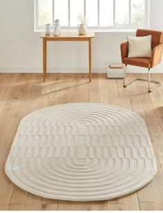 a chair and table in a room with hardwood floors, white rugs and windows