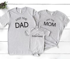 two shirts with the words first time dad and baby on them, next to a plant