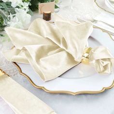 an elegant table setting with white and gold plates, napkins, and silverware