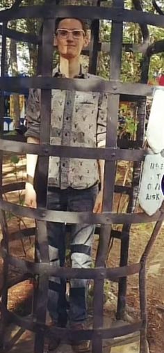 a man standing behind a metal cage in the woods