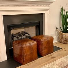 two leather ottomans sit in front of a fireplace with a potted plant next to it