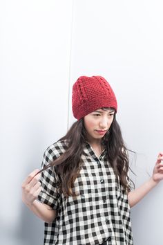 a woman wearing a red knitted hat with her hands in the air while standing against a white wall