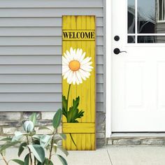 a welcome sign on the side of a house next to a white door with a flower painted on it