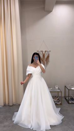 a woman taking a selfie wearing a white wedding dress with off the shoulder sleeves