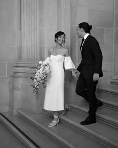 a bride and groom walking up the steps together holding hands in black and white photo