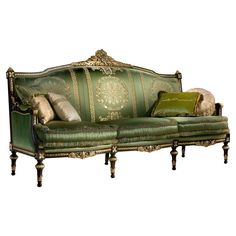 a green couch with pillows on it and gold trim around the armrests, sitting in front of a white background