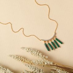 Description : Inspired by the beautifully patterned Malachite gemstone, the earliest ore of copper, Tamra is eccentric, contemporary, and distinctively classy. Handcrafted on 925 hallmark silver and gold finish. This collection is curated for everyday luxury.This minimal charm necklace features a line charm studded with CZ stones. Five malachite charms are suspended from the chain for a striking everyday style. Product Information : Materials used: 925 Silver with Gold & White Gold Plating Stone Gold Emerald Necklaces With Gemstone Beads, Handmade Gold Malachite Necklaces, Handmade Gold Necklaces With Malachite, Minimalist Brass Necklace With Gemstone, Handmade Gold Necklace With Malachite, Minimalist Brass Gemstone Necklace, Modern Green Jewelry With Gemstone Accents, Gold Malachite Gemstone Necklace, Gold Malachite Jewelry For May Birthstone