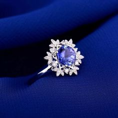 an oval shaped tanzante and diamond ring sits on a blue fabric with white diamonds surrounding it