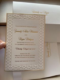 a person holding up a white and gold wedding card