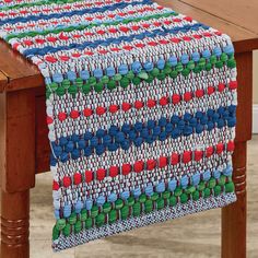 a wooden table topped with a multicolored knitted table runner