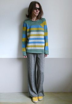 a woman standing in front of a wall wearing striped sweater and pants with yellow shoes