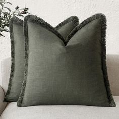 two green pillows sitting on top of a white couch next to a potted plant