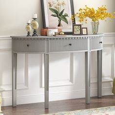 a grey console table with flowers and pictures on the top, in front of a white wall