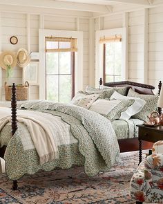 a bedroom with a large bed covered in floral comforter and pillows, along with two windows