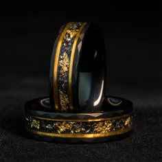 two wedding rings with gold and black designs on each one, sitting side by side