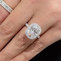 a woman's hand with two engagement rings on her finger and the ring has an oval shaped diamond surrounded by smaller diamonds