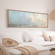 a painting hanging on the wall above a white couch and ottoman in a living room