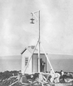 an old black and white photo of people working on a small house near the ocean