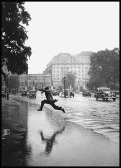 a person jumping in the air while holding an umbrella on a rainy day with cars and buildings in the background