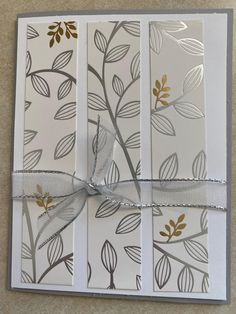 a white card with gold leaves on it and a ribbon tied around the front of it