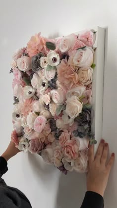 a woman is placing flowers on the wall to decorate an art piece with her hands