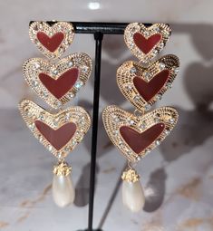 These stunning heart-shaped earrings feature three delicate hearts, gracefully dangling from a captivating gold outer interior with rhinestones for that extra sparkle. Adorn yourself with timeless beauty and express your love with every sway. Elegant Heart Pendant Earrings For Party, Elegant Heart Earrings For Party, Elegant Rose Gold Heart Earrings, Elegant Metal Earrings With Heart Beads, Valentine's Day Rose Gold Heart Earrings For Party, Elegant Metal Heart Earrings For Valentine's Day, Glamorous Double Heart Jewelry For Parties, Heart Pendant Metal Earrings For Party, Party Earrings With Heart Pendant In Metal