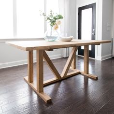 a wooden table sitting on top of a hard wood floor next to a window with white curtains