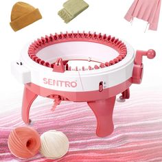 a pink and white spinning machine with two balls of yarn next to it on top of a bed