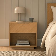 a nightstand with books and a cup on it next to a bed