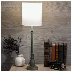 a lamp on a table next to books and a vase with dried grass in it