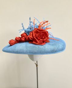 "A stunning pale blue and orange wide brim hatinator.  This gorgeous statement headpiece is made using sinamay straw in a beautiful shade of powder blue. Central to this hat, is a  large handmade silk dupion rose in burnt orange and five matching rose buds that cascade down the brim to one side.  A small collection of powder blue and orange feathers float out  from the top of the rose, adding movement and drama to the overall finished hat.  This particular design has a shallow brim and is secured with a double metal headband that it ribbon wrapped in a colour to blend in with your own hair colour. This band is completely invisible when the hat is on.  Measuring 44cm side to side and 37cm front to back. It is made to a standard 22\" diameter, however, if you require a smaller fit I can prov Blue Fascinator With Handmade Flowers For Kentucky Derby, Blue Handmade Flowers Fascinator For Races, Blue Fascinator For Royal Ascot Garden Party, Blue Fascinator For Garden Party And Royal Ascot, Blue Fascinator For Garden Party At Royal Ascot, Blue Mini Hats With Handmade Flowers For Royal Ascot, Blue Feathered Summer Costume Hats And Headpieces, Blue Feathered Fascinator For Summer, Blue Feather Fascinator For Summer