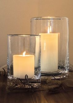 two lit candles sitting on top of a table next to each other in glass vases