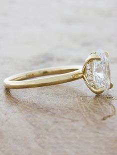 a yellow gold engagement ring with a pear shaped diamond in the center on a wooden surface