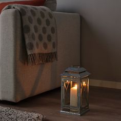 a lit candle sitting on the floor next to a couch with a throw blanket over it