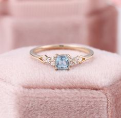 a ring with an aqua blue topaz surrounded by white diamonds on a pink velvet box