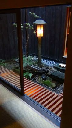 a lamp that is on in the middle of a room next to a pond with rocks and plants