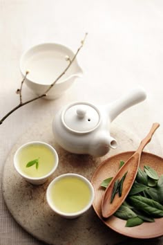 a tea pot and two cups filled with green tea sit on a plate next to some leaves