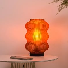 an orange lamp sitting on top of a white table next to a potted plant