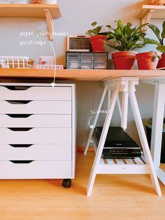 an office desk with drawers and plants on the top shelf, along with other items