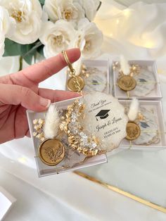 a person holding some gold and white items in front of flower arrangements on a table