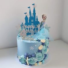 a frozen princess cake with blue frosting and flowers on top, sitting in front of a white wall