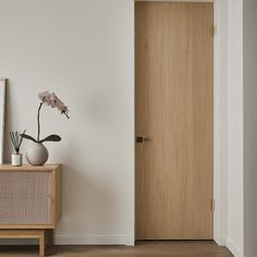 a vase with a flower in it sitting next to a wooden door on a white wall