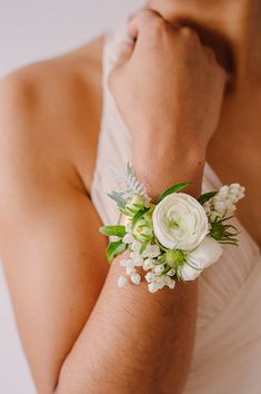 a close up of a person wearing a white flower wrist corsage with green and white flowers