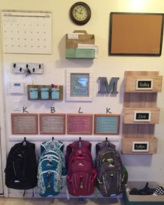 several backpacks are lined up on the wall in front of a clock and calendar