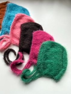 four different colored knitted hats sitting on top of a white table next to each other