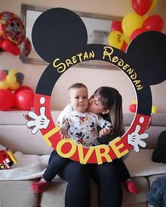 a woman holding a baby in front of a mickey mouse frame with the words love on it